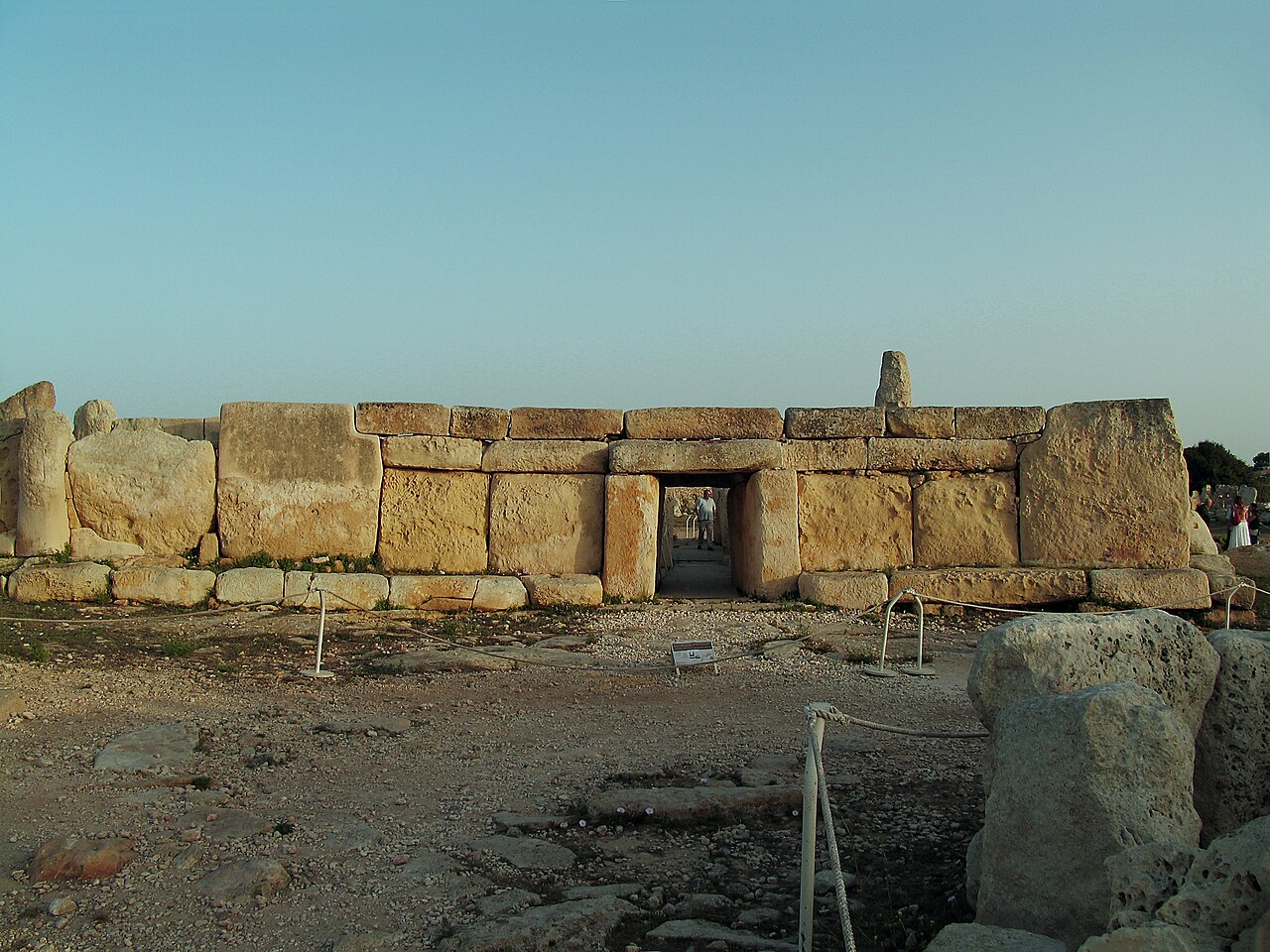 The curved megalithic façade of Ħaġar Qim, with its trilithon doorway, under a clear sky.